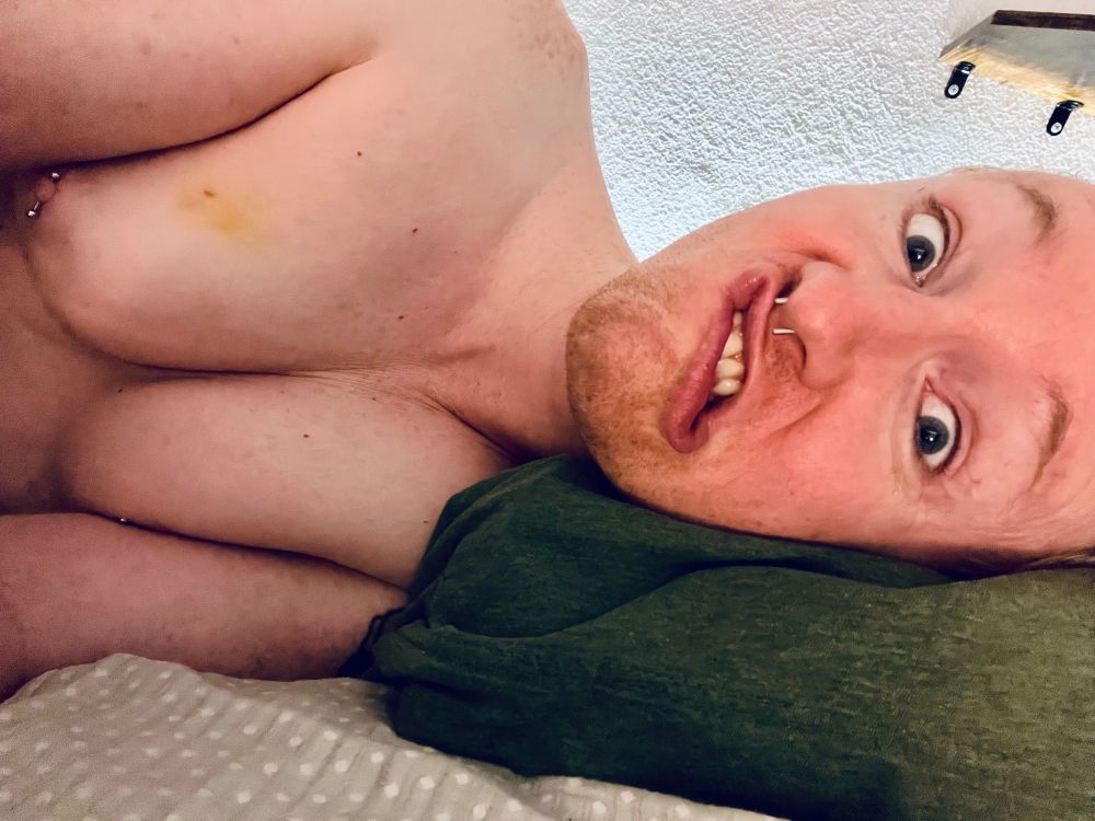 Fox lying naked in its bed, visible from bust up. her tits are plump and showing some cleavage as she lays on her side. she is making a silly face with eyes wide and lips pulling in opposite directions, showing a little bit of teeth.