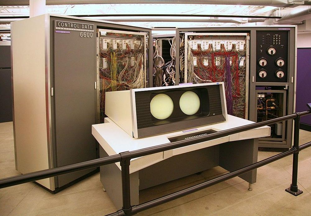 Picture of a Control Data Corporation CDC660. Two arms of the plus-shaped machine are visible, each arm looks like a double wide full height rack. 
In front there is a terminal with two round screens that is built into a desk.

 One of the first supercomputers and was introduced in 1964.