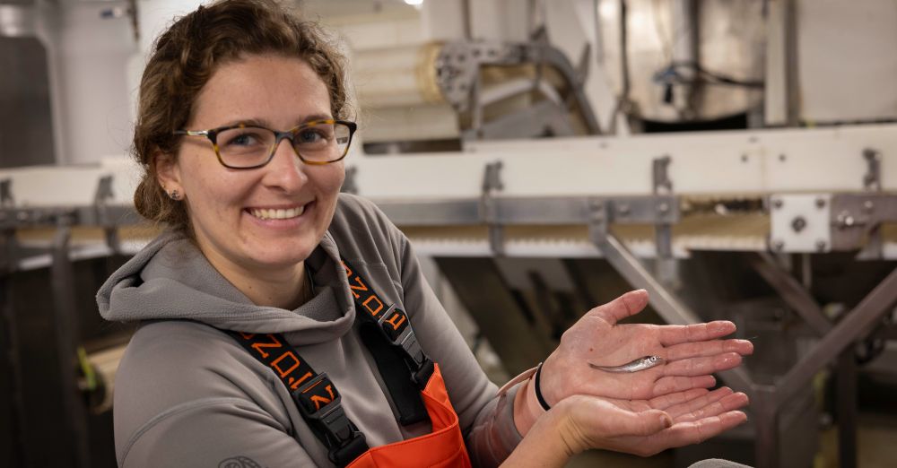 Smiling woman holds small fish in outstretched hands toward the camera.