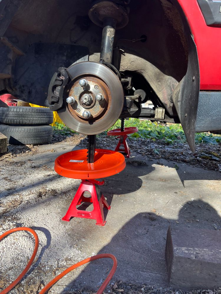 A close up of the jack stands at the front, showing how I’m using paint bucket lids to hopefully deter mice from climbing them