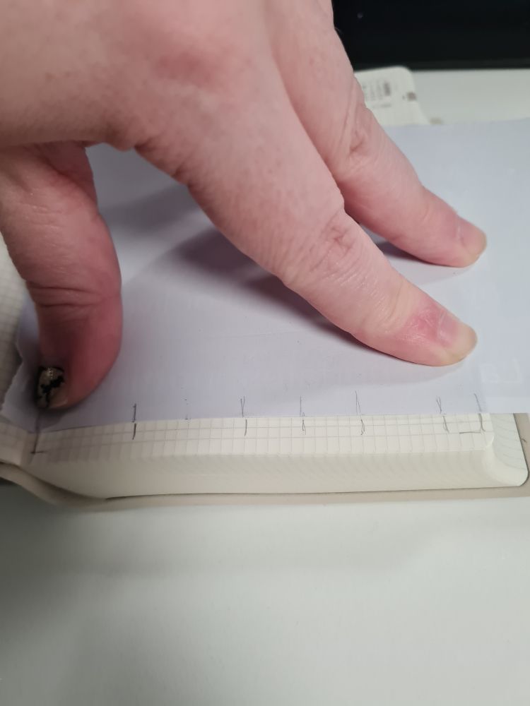 A piece of scrap paper on a page of blank squared paper. The edge of the paper has pencil markings that line up with the columns, and pencil lines are drawn on the page to match.