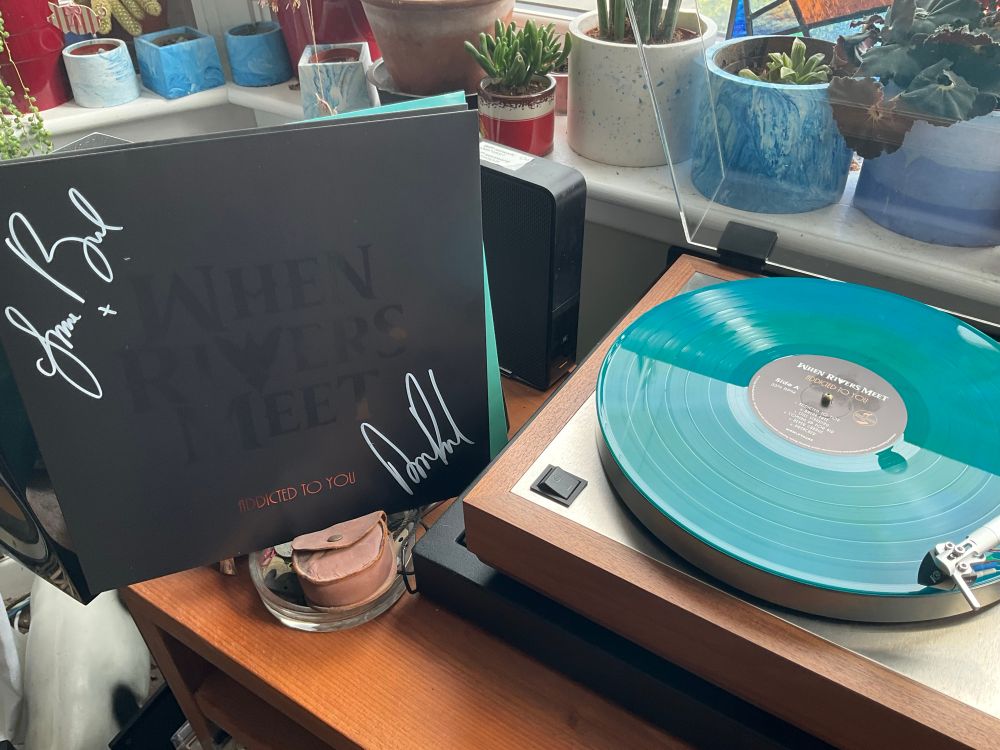 Gatefold sleeve leaning next to turntable with turquoise record playing. Front cover signed by Grace and Aaron Bond