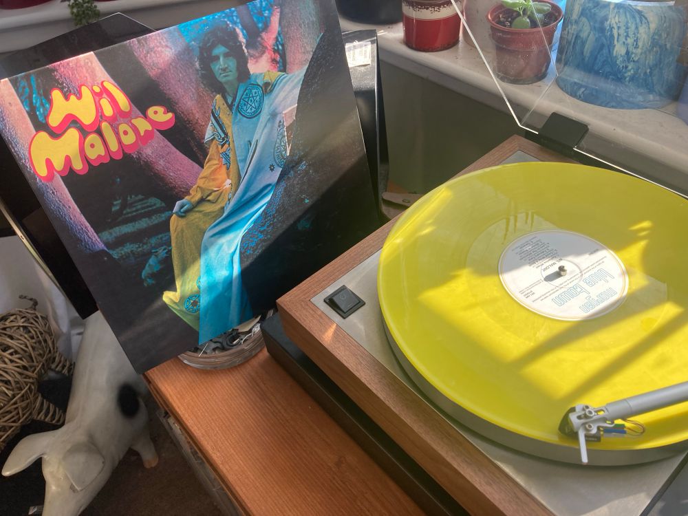 Bright yellow coloured vinyl record playing on a turntable with the album cover leaning against the turntable