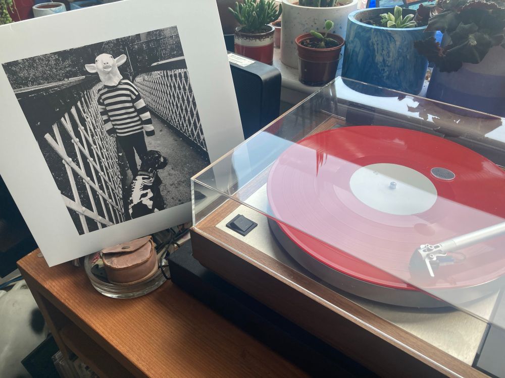 Photo of album cover stood next to the turntable playing the red vinyl version of the album.