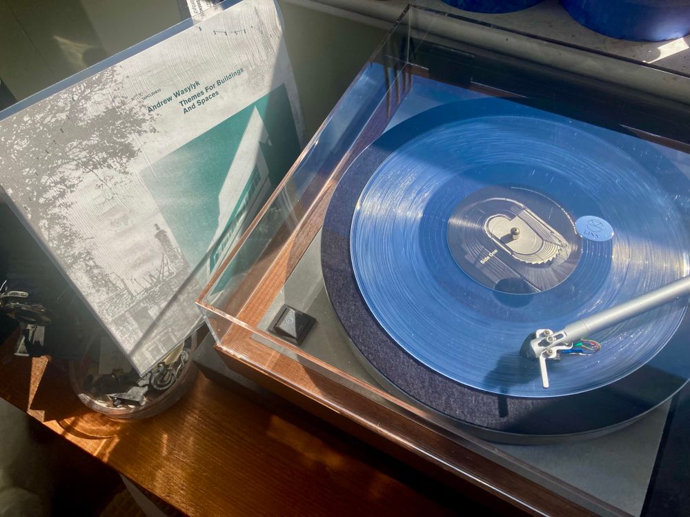 10” album cover leaning on old cameras next to a Linn Sondek LP12 turntable with 10” clear vinyl (66 of 80) playing on turntable