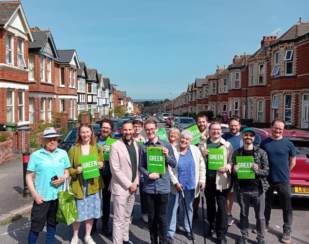 Deputy leader Zack Polanski in a terraced street in Exeter with Thomas Richardson and eleven others. Some are holding posters reading "I'm voting Green."