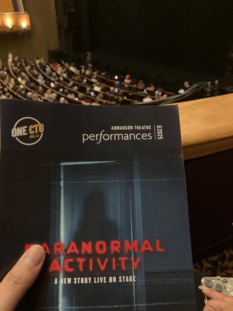 In a theatre a program booklet of the stage play Paranormal Activity, yes it exists, is on screen but a thumb is blocking the P and A. 