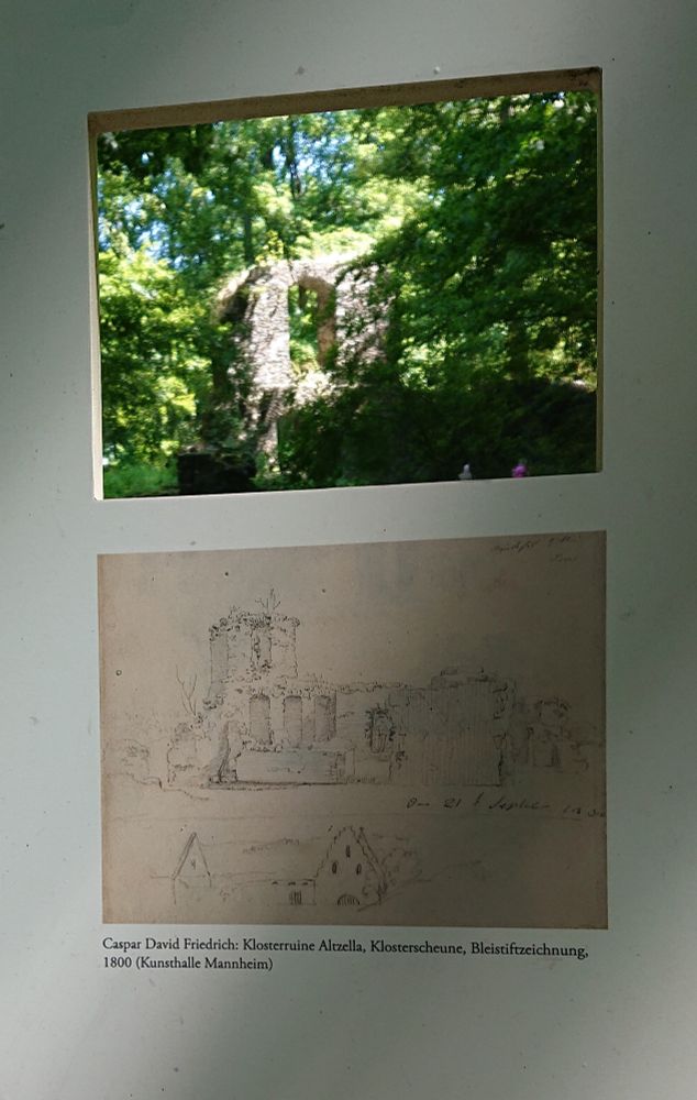 Ein Teil einer Schautafel. Durch ein rechteckiges Loch oben sieht man eine Ruine. Darunter ist eine Sepiazeichnung dieser Ruine abgebildet. 