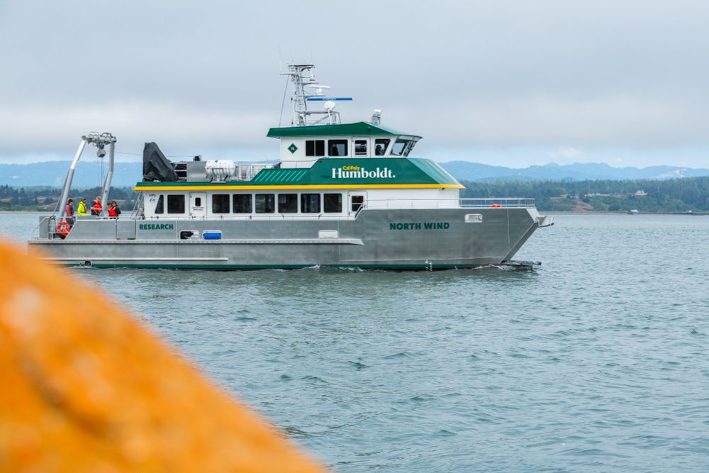The research vessel North Wind cruises in Humboldt bay with a few people on the rear deck. 