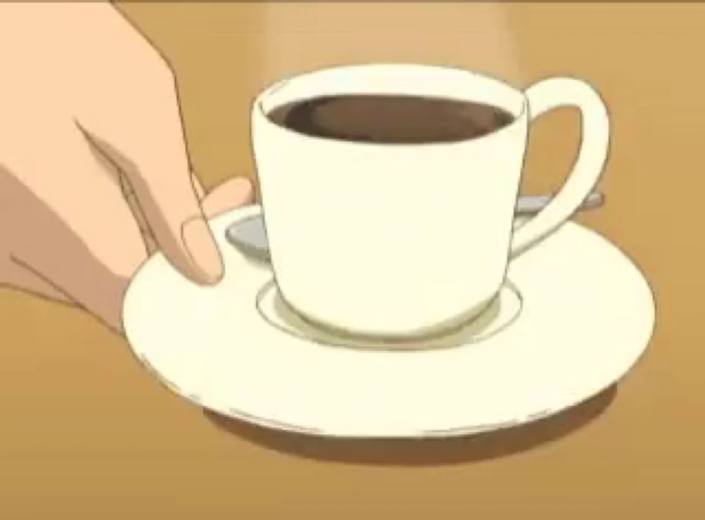 a person is holding a cup of coffee on a saucer on a table .