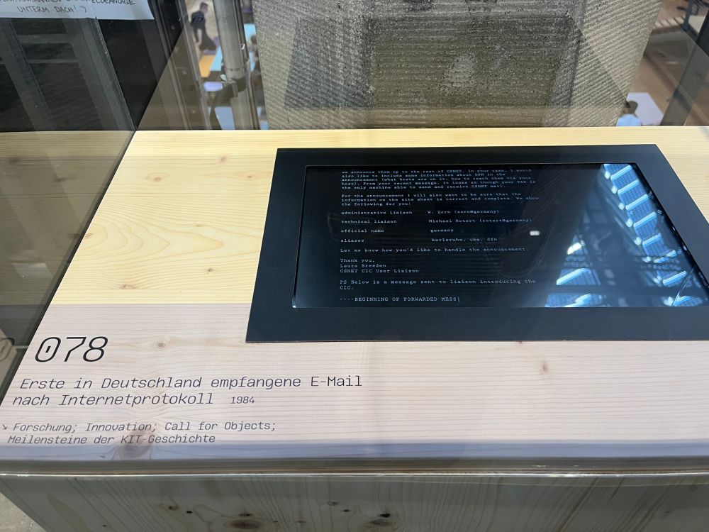 Ein waagrecht liegender Bildschirm in einer Vitrine mit dem Text der ersten ind Deutschland empfangenen E-Mail nach Internetprotokoll. Daneben ein Text mit ebendieser Beschreibung.