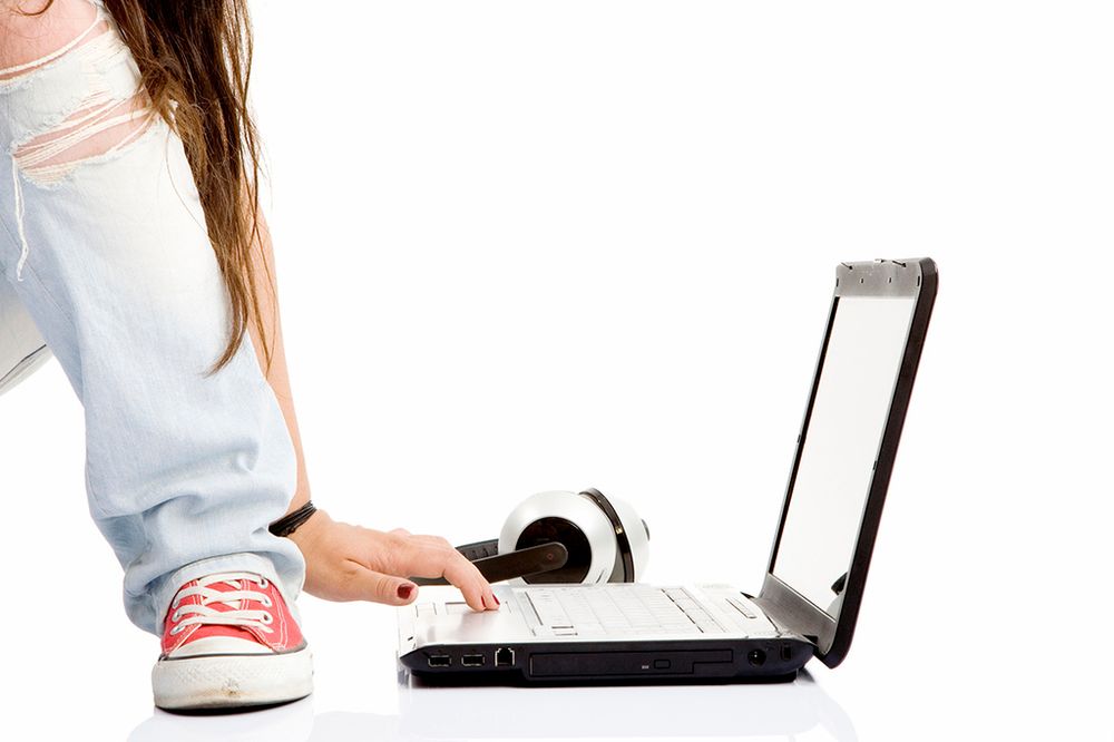 Symbolfoto mit einem geöffneten Laptop und einem Kopfhörer auf dem Boden. Davor sieht man ein Bein vom Schuh bis zum Knie und merkwürdig verdreht eine Hand, die auf der Tastatur ruht.