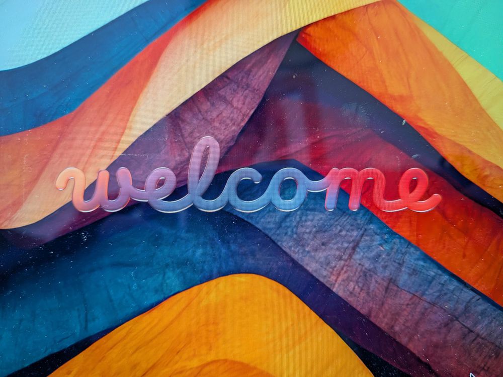 Screenshot of the liquid glass "welcome" joined-up text, that looks kind of pretty on my very colourful background but also somewhat tricky to read.