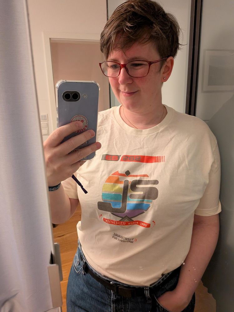 Sara taking a mirror selfie. She's wearing an off-white T shirt with a JS logo reminiscent of blank video-cassette cover graphics of the 90s.