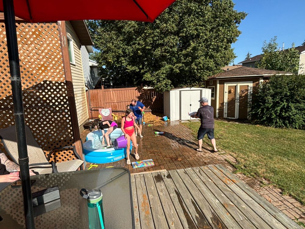 Kids and adults in a backyard with a paddling pool full of water balloons and water guns!