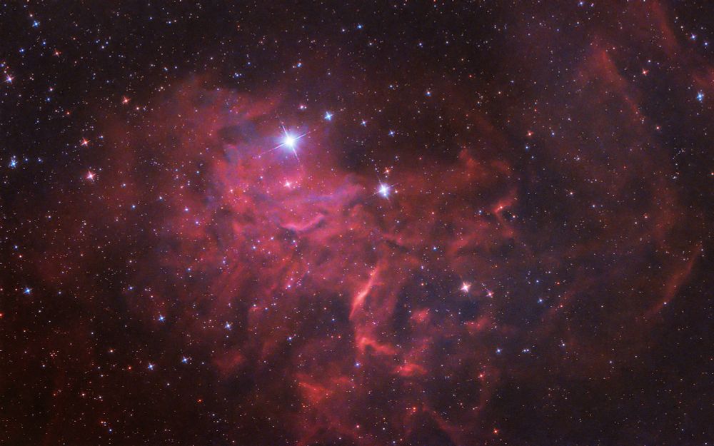 An image of a red emission nebula with a bright star in the middle 
