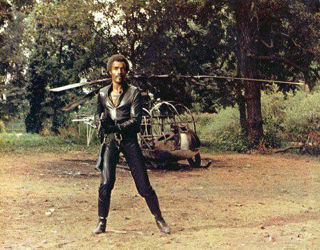 Calvin Lockhart wearing black leather and holding a machine gun in The Beast Must Die