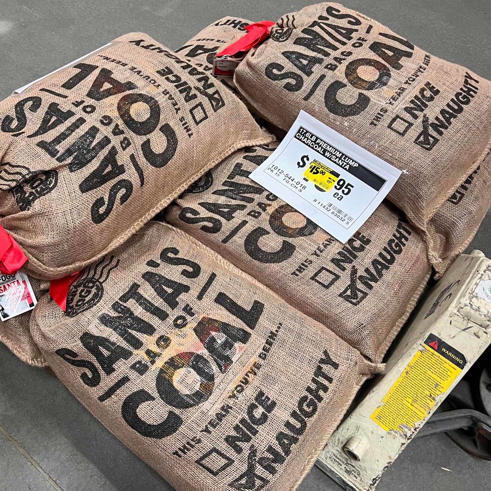 Skid piled with large, full, price-discounted canvas bags labeled “Santa’s Bag of Coal”.