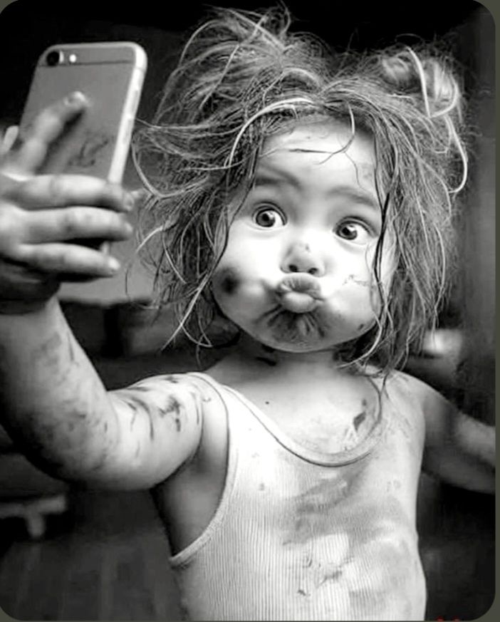 A black and white photo of a little girl making a kiss face for a selfie.