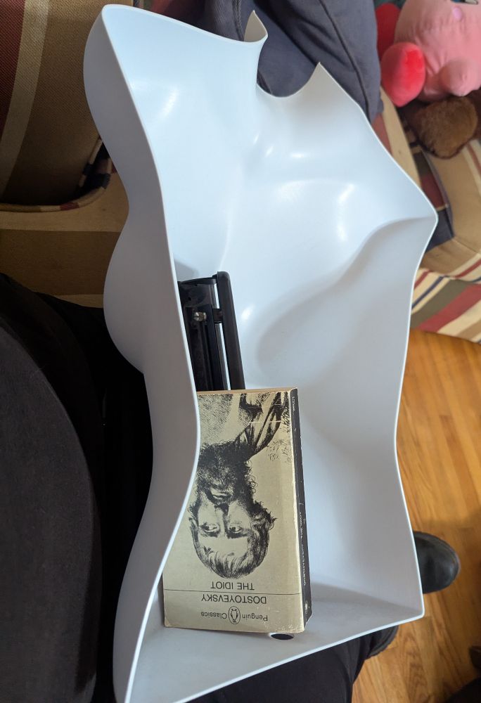 a plastic half-torso turned over, being used to contain a three-hole punch and a penguin classics copy of "the idiot" by Dostoyevsky.