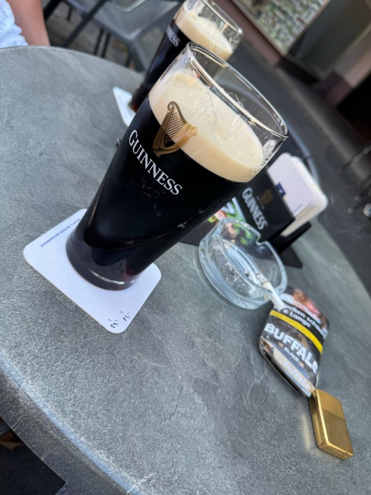 Kneipentisch draußen. Ein Feuerzeug, ein Tabaksbeutel und zwei Gläser Guinness n