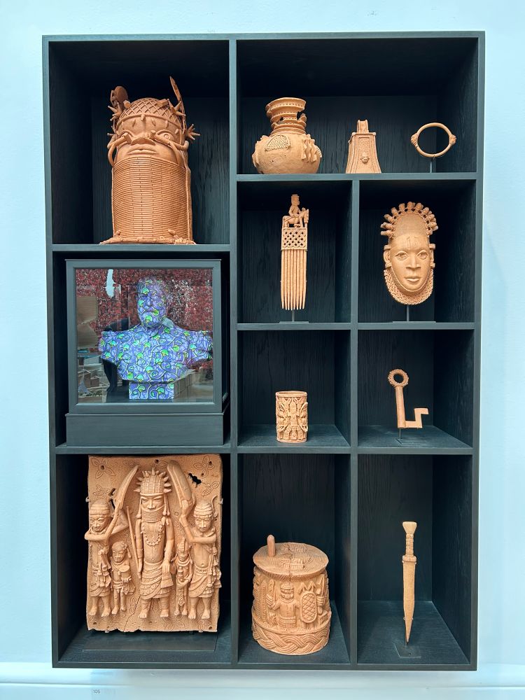 Rectangular wood shelf with 11 terracotta replicas of Benin Bronzes and a bust of a British man. https://se.royalacademy.org.uk/2025/artworks/yinka-shonibare-ra/105