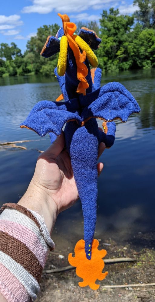 a blue dragon from the top/back, showing off the tail tuft and paint details, the wing embroidery/form, as well as the tops of their big yellow ram horns