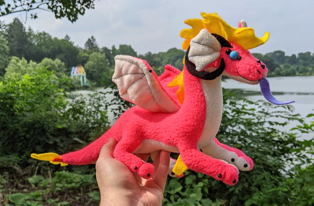a bright neon pink dragon with a white underbelly/inner ears/underwings, purple tongue, yellow mane/tail/elbow tufts, black horns/claws/markings, sky blue eyes