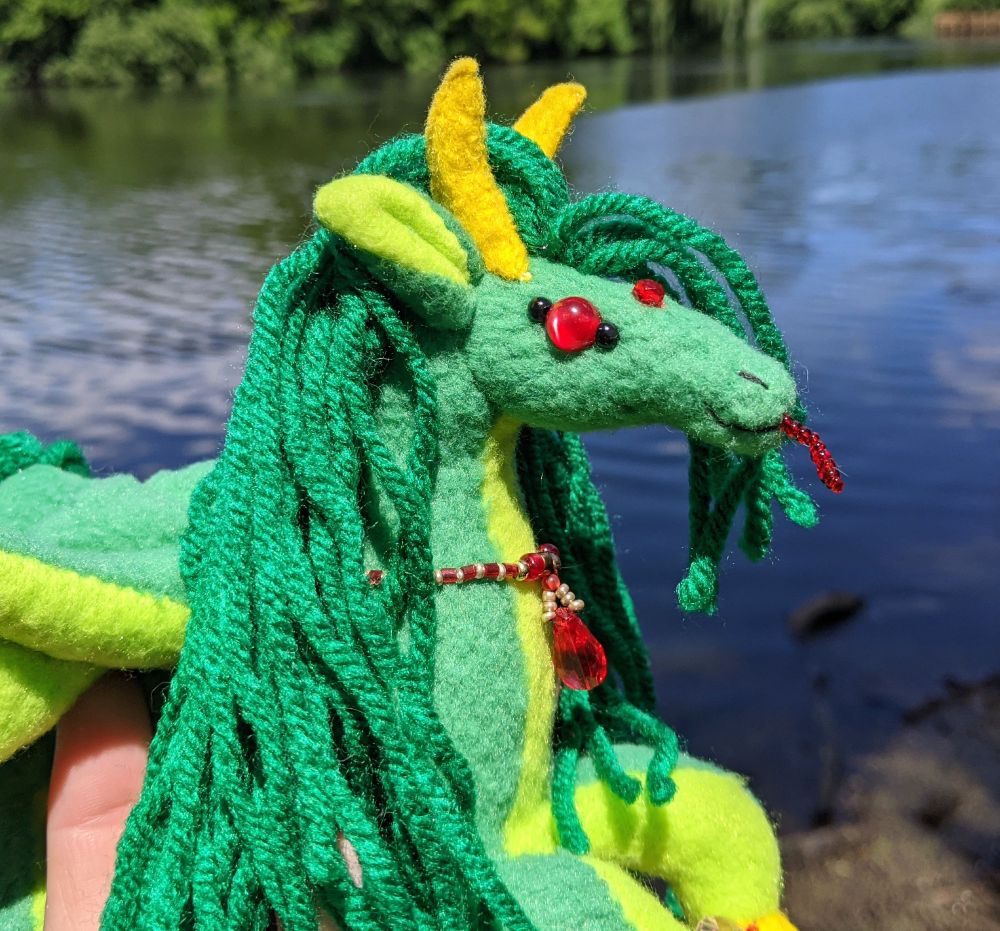 closeup of their face. showing off the green/yellow/red color scheme, showing off some of the depth in the catseye bead eyes, and the bright red beaded tongue