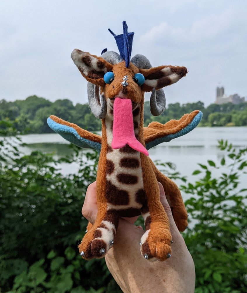 a warm brown dragon with a dark brown/cream patterned underbelly and inner ears, sky blue underwings, dark brown mane/tail/elbow tufts, gray/silver claws/horns/markings, a bright pink tongue, and sky blue eyes