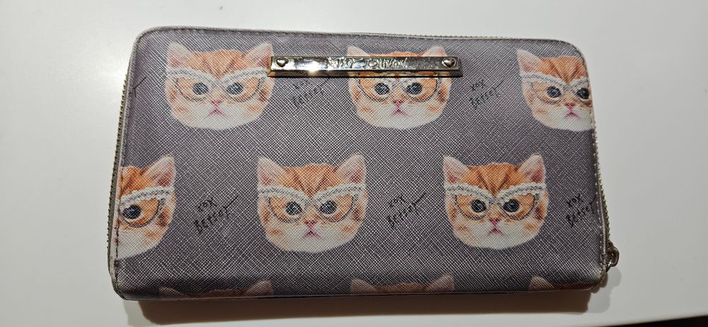 Photo of a grey Betsy Johnson wallet with a pattern of a oraneg tabby cat face wearing a pair of cats-eye glasses