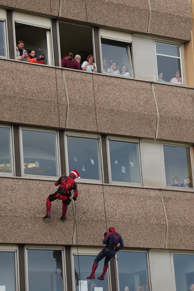 super héros, Spiderman,  descendent en rappel la façade de l'hôpital pour enfants avec des personnes aux fenêtres