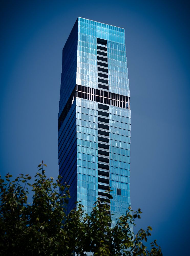 A ground level shot of the Residences at St. Regis along the Chicago River.

The top third of the tallest of its 3 towers is visible above a tree’s canopy. 