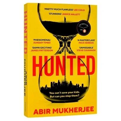 A yellow book with the title, HUNTED in red upper case letters on the front and spine. The author's name, Abir Mukherjee is also in red letters on the front cover, with is dominated by and hour glass, with a single figure standing in the top half and the sand running through to create a cityscape in the bottom half. 