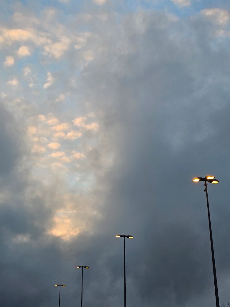 Straßenlaternen vor bedecktem Morgenhimmel.