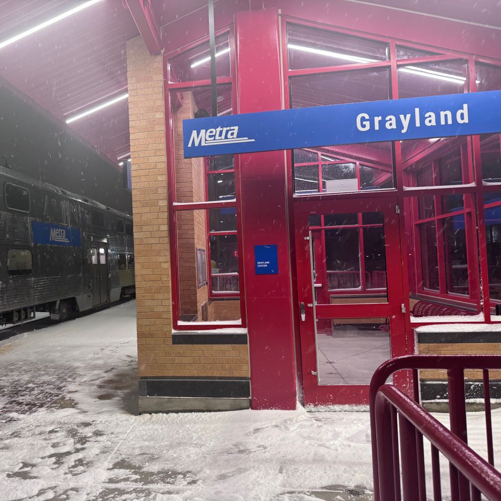 Grayland Metra station shelter on northbound platform. Small building with tan brick and red trim. 
