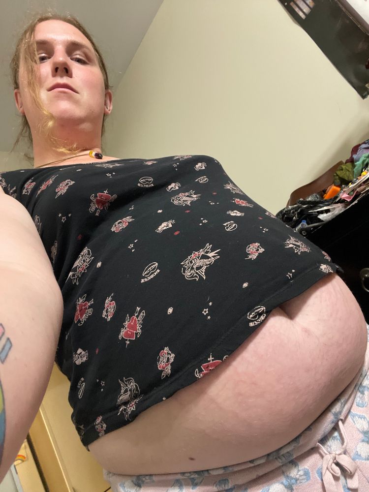 A selfie of Lyra with a low angle taken at her waist showing off her large tummy poking out under a tank top and over sleep pants while Lyra looks down at the viewer.