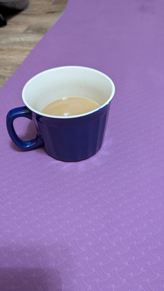1/2-full cup of coffee sitting on a purple yoga mat, on the floor.