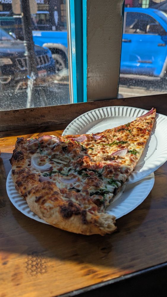 Slice of pizza on a wooden counter, by a window.