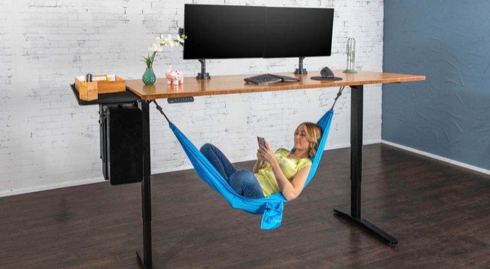 Woman laying in blue hammock that is suspended under a raised standing desk.