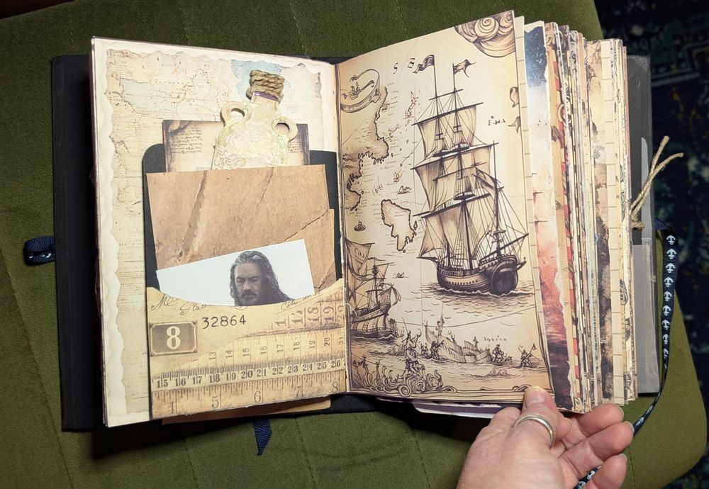 The journal lays open on the left page is an envelope with a photo of Ed Teach and paper bottle peaking out on the left page and a drawing of a pirate ship on the right page.