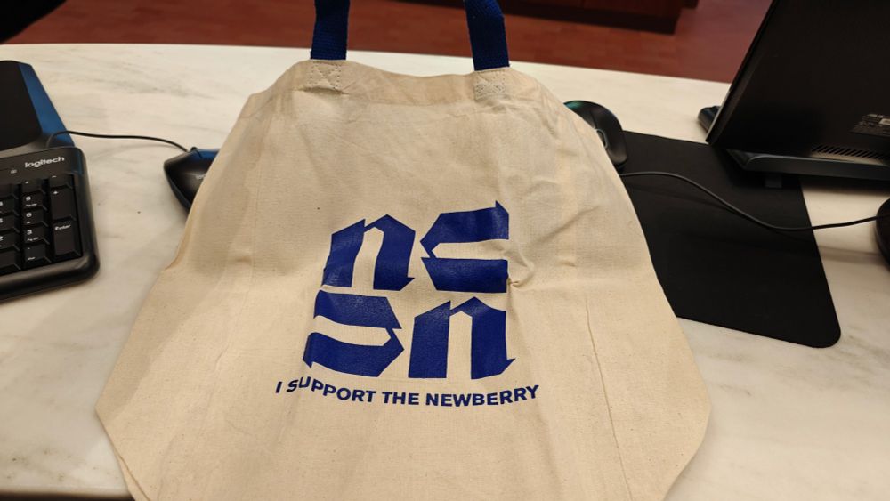 An off white tote bag with the Newbury Library logo in blue