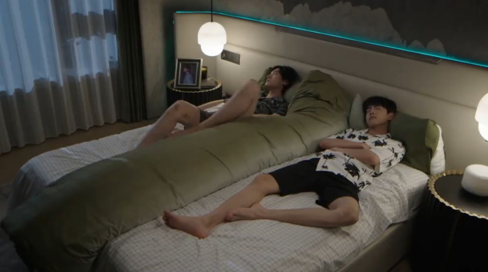 A screenshot from Revenged Love episode 20 of Guo Chenyu and Jiang Xiaoshuai lying in bed together separated by a gigantic green body pillow.