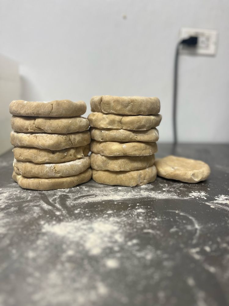 Work station covered in flour with 13 discs of formed pie dough in the background 
