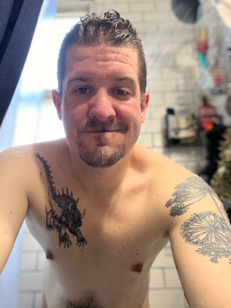 Tattooed wet torso looking out from the shower 