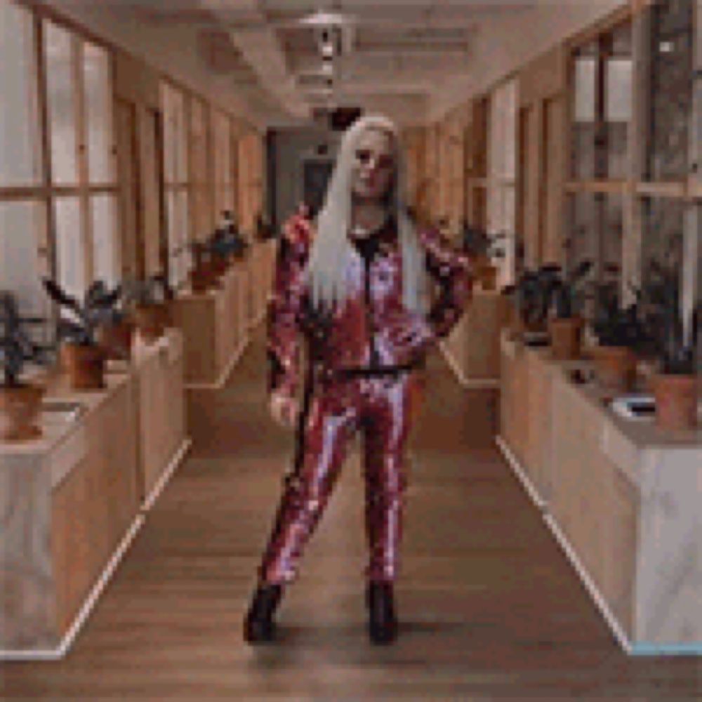 a woman with long blonde hair is walking down a hallway in a sequined suit .