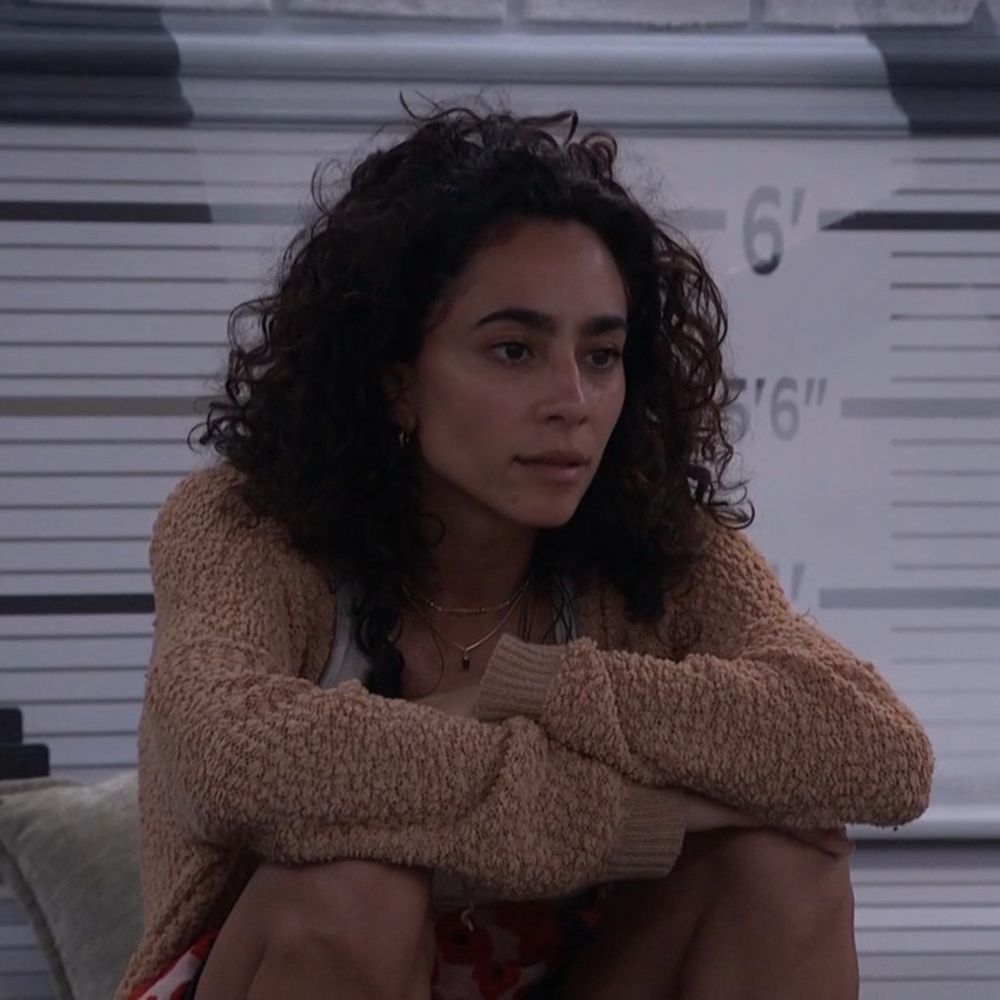morgan from big brother season 27 — a lightskin brown woman with shoulder length curly hair. she is crossing her arms while resting elbows on knees, she is wearing brown fuzzy sweater. 