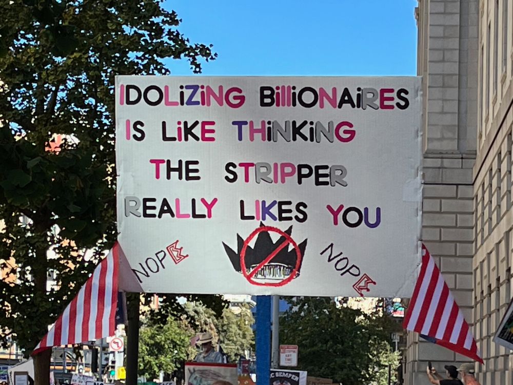 A sign says "Idolizing billionaires is like thinking the stripper really likes you"