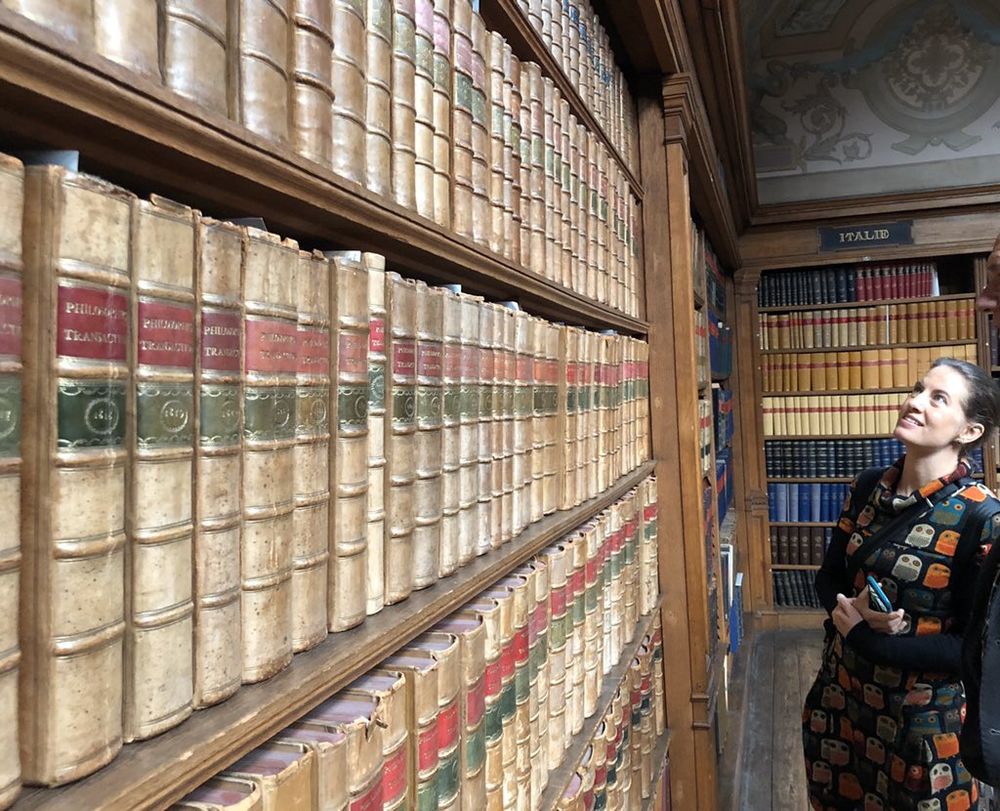 A woman standing in front of a bookshelf filled with historic bound journals
