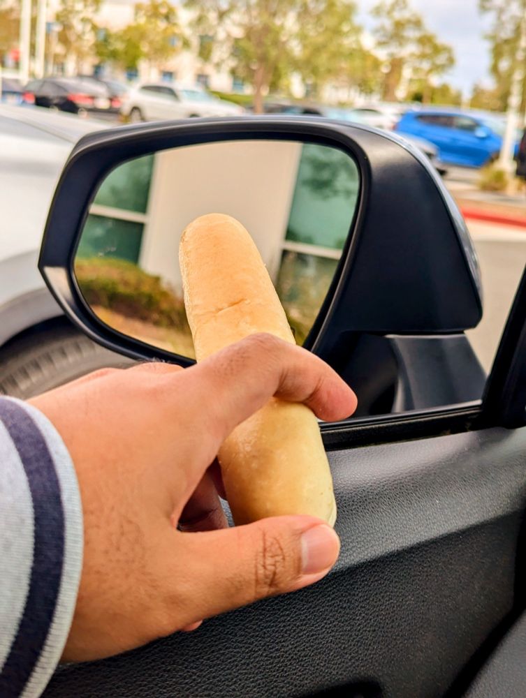 An Olive Garden bread stick being held outside a car window like a cigar